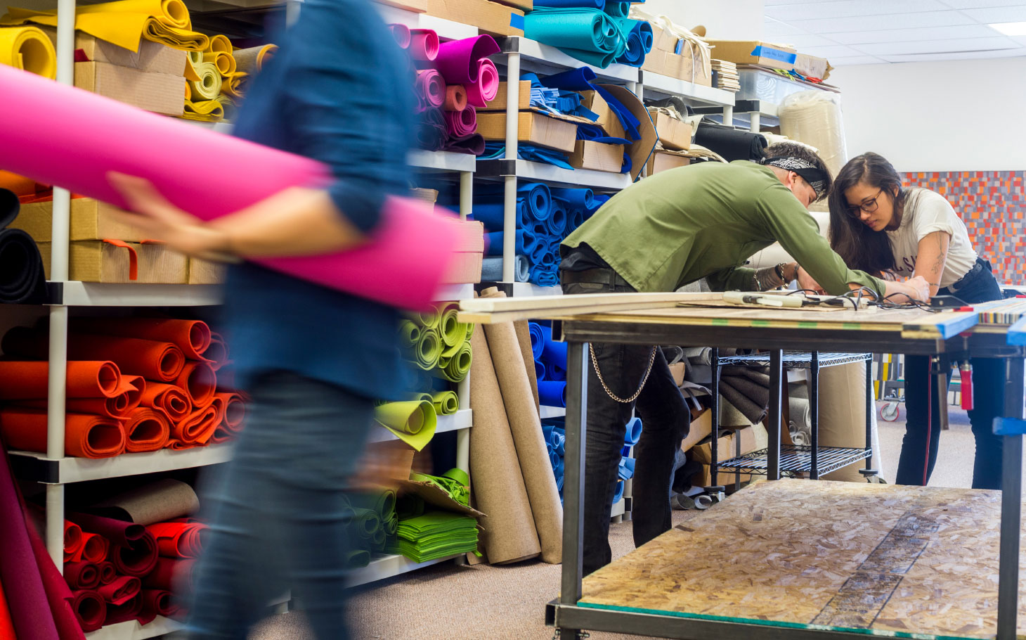 Three people working in a space with work tables and shelves of felt.