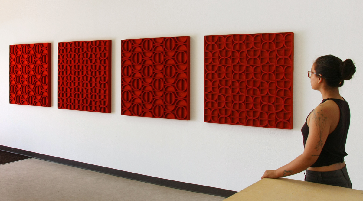 A women looks at four square red felt wall panels with different patterns