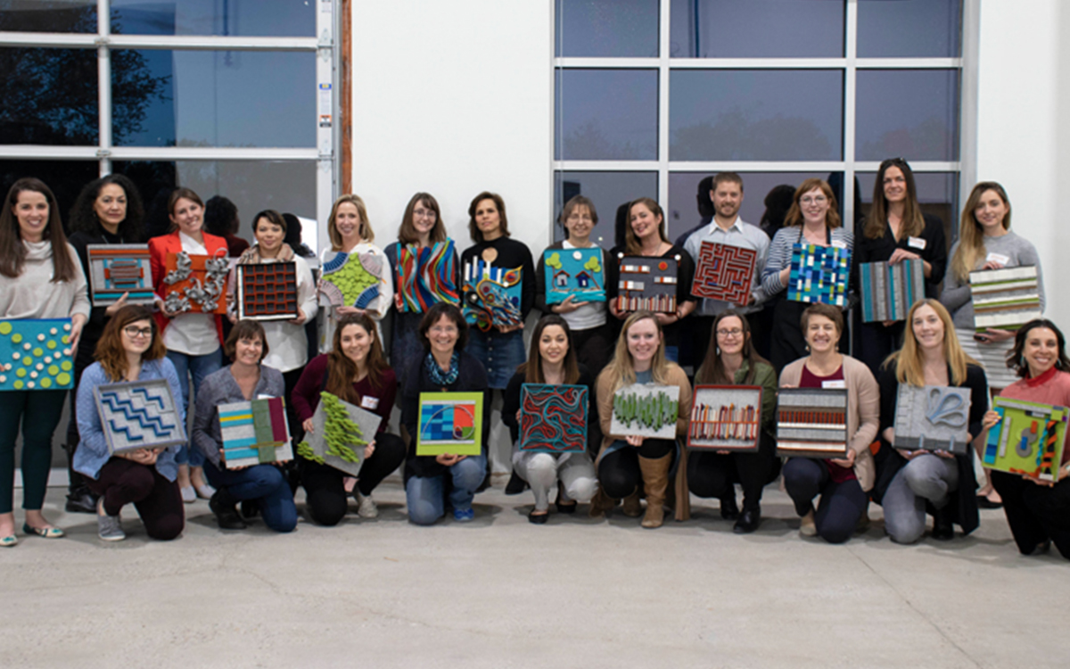 Two rows of people holding felt tile designs and smiling