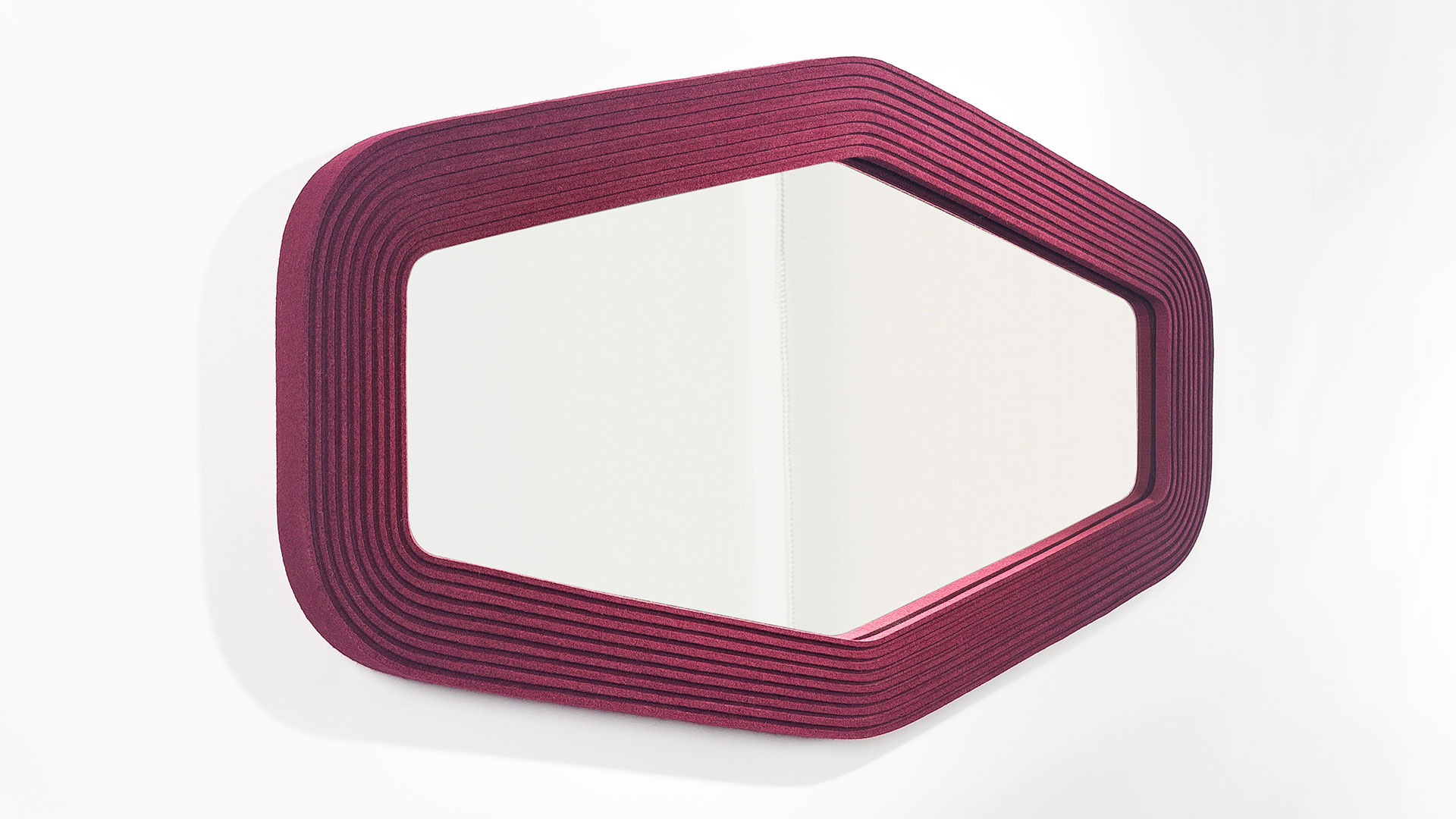 A hex shaped mirror framed with deep red ribbed felt hung horizontal