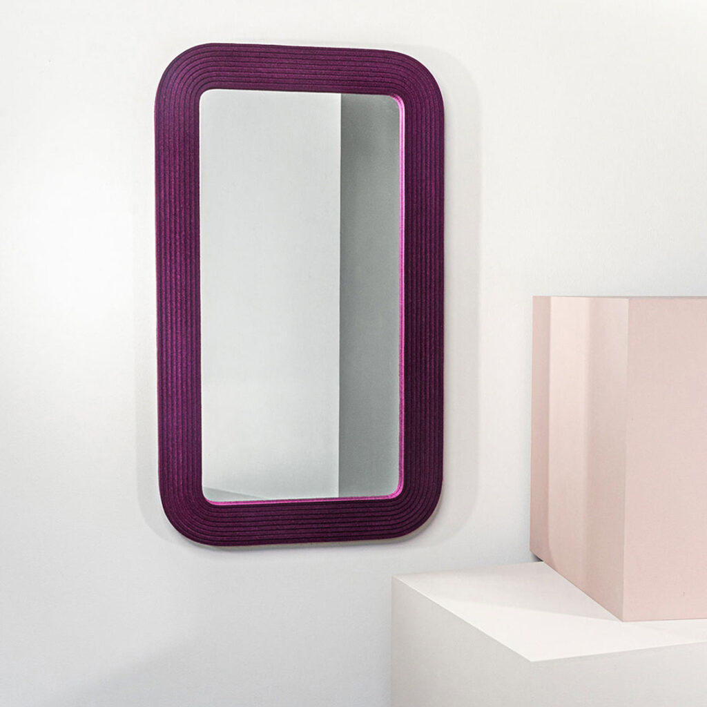 A rectangle mirror framed with deep red/purple ribbed felt hung vertical next to a pink and white box