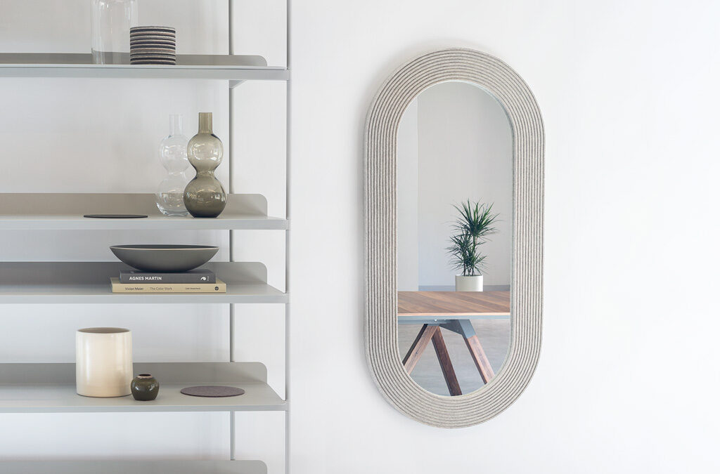 Pill shaped mirror make with heathered gray felt next to a shelf unit with knickknacks