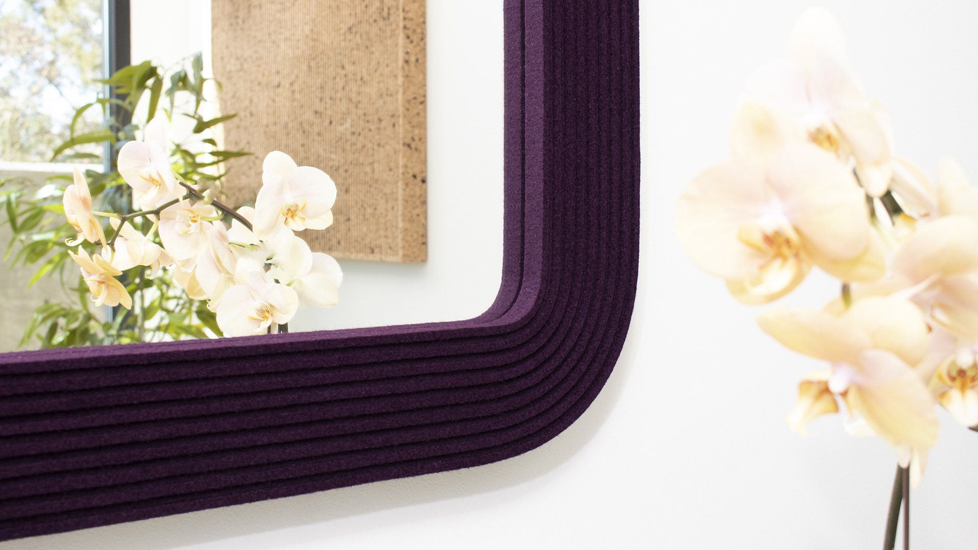 Corner of a eggplant colored wood felt frame of a square mirror with orchid
