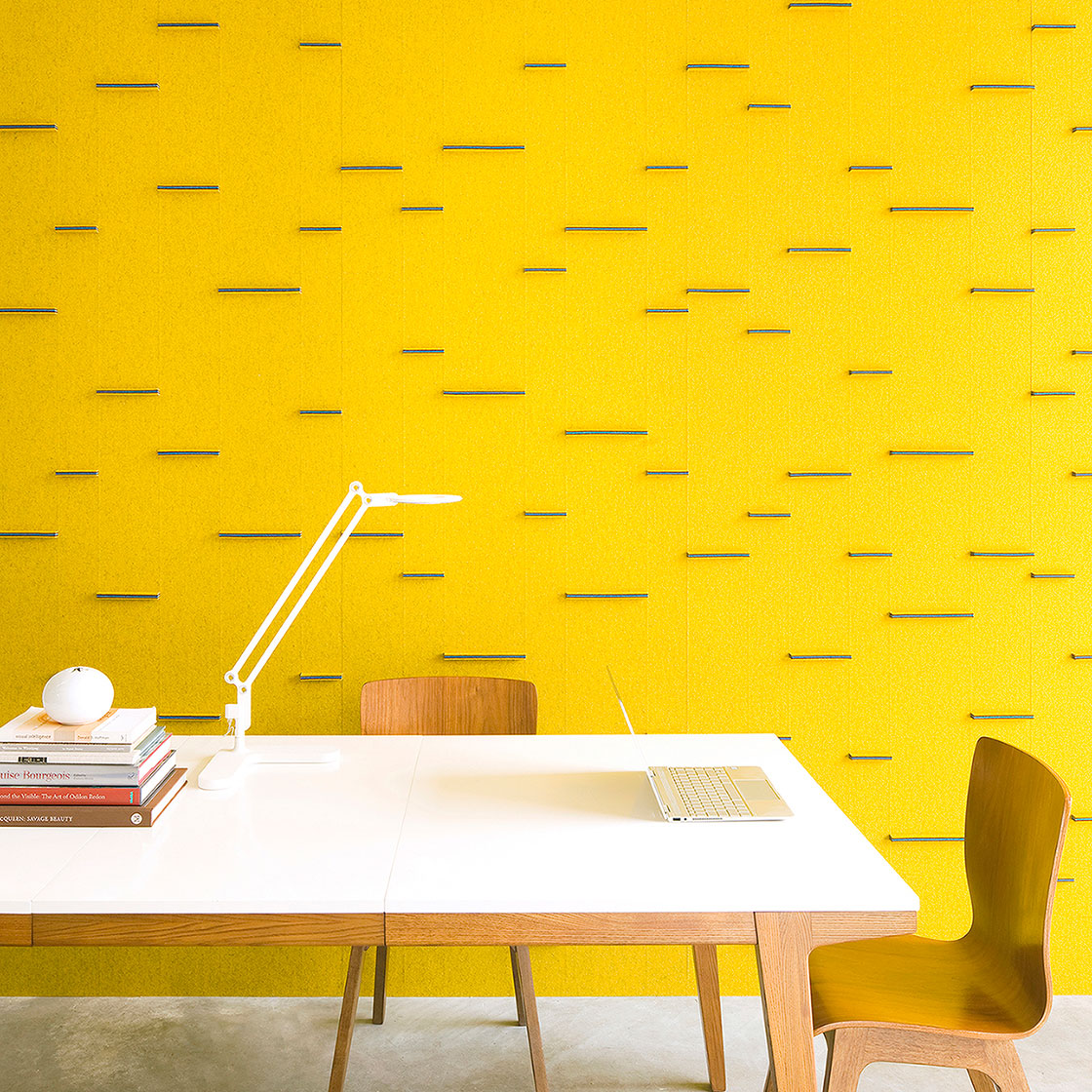 A room scene with a table used as a desk in front of a bright yellow wool felt wall with blue horizontal tabs in various legnths