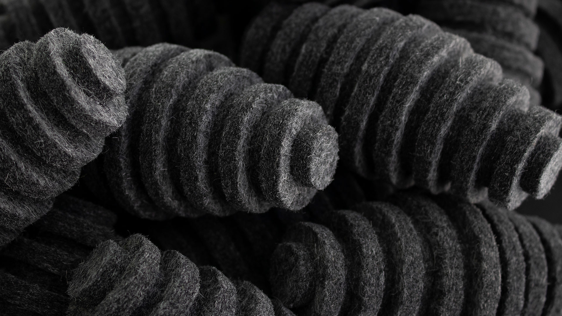 Closeup of pile of dark gray felt pods. They are oblong egg-shaped and have ridges.