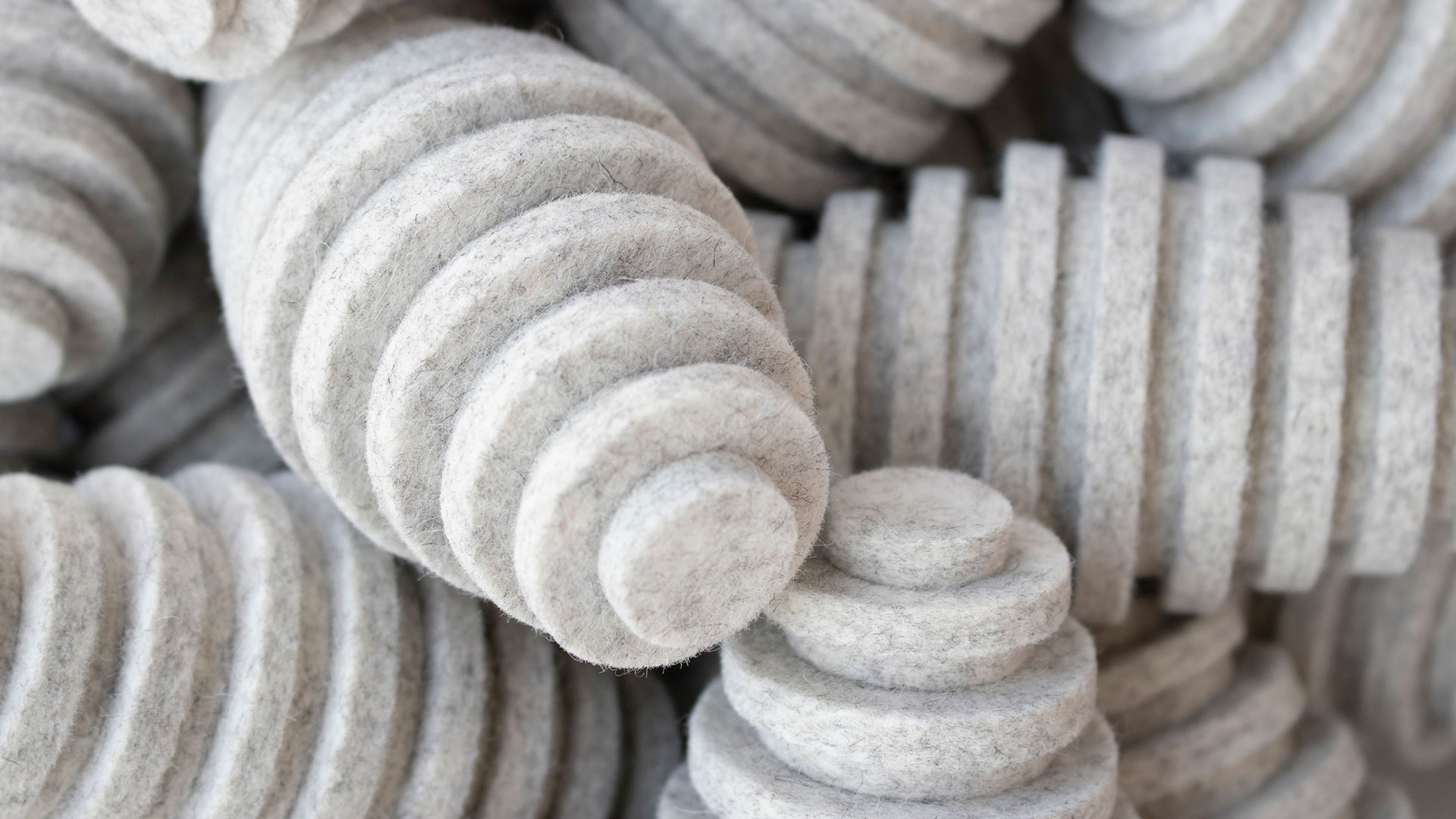 Closeup of pile of heathered white felt pods. They are oblong egg-shaped and have ridges.