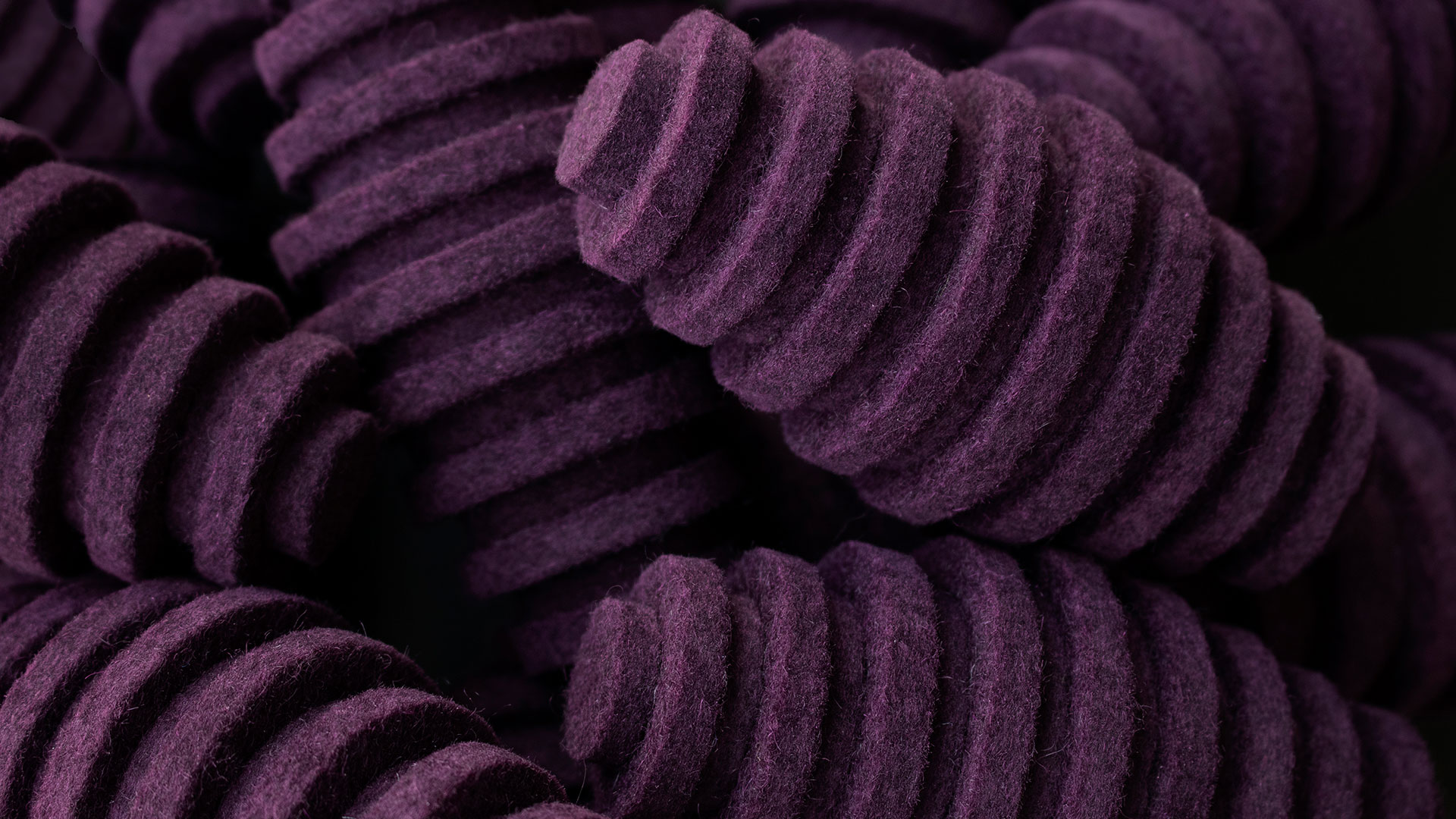 Closeup of pile of purple felt pods. They are oblong egg-shaped and have ridges.
