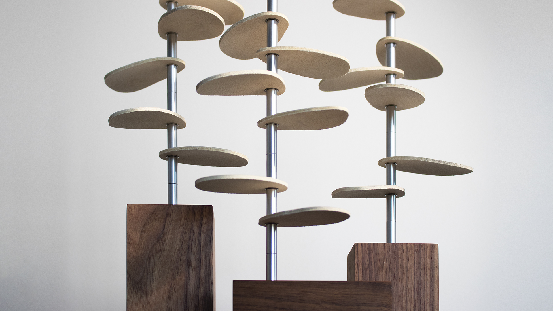 Closeup of trio of tree-shaped design pieces with wood bases, metal stems, and white leather leaves.