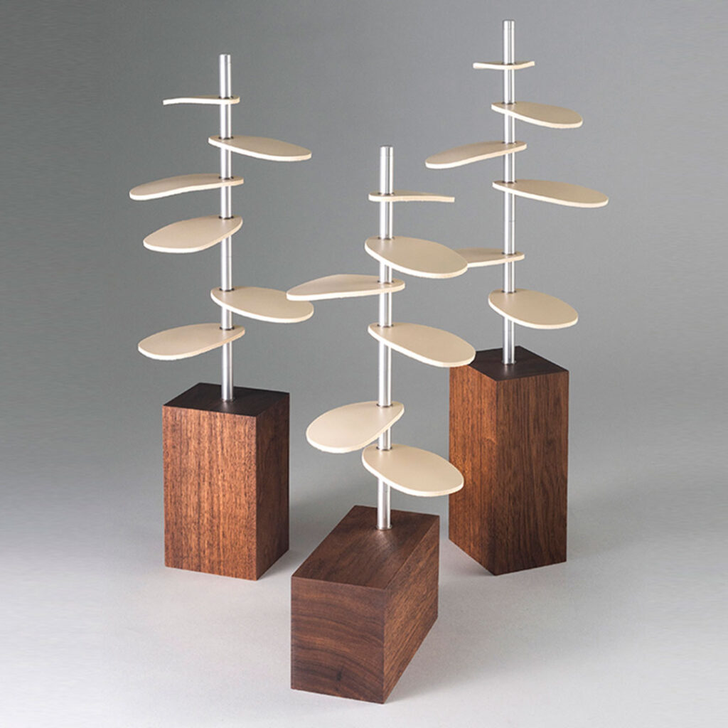 trio of tree-shaped design pieces with wood bases, metal stems, and white leather leaves.