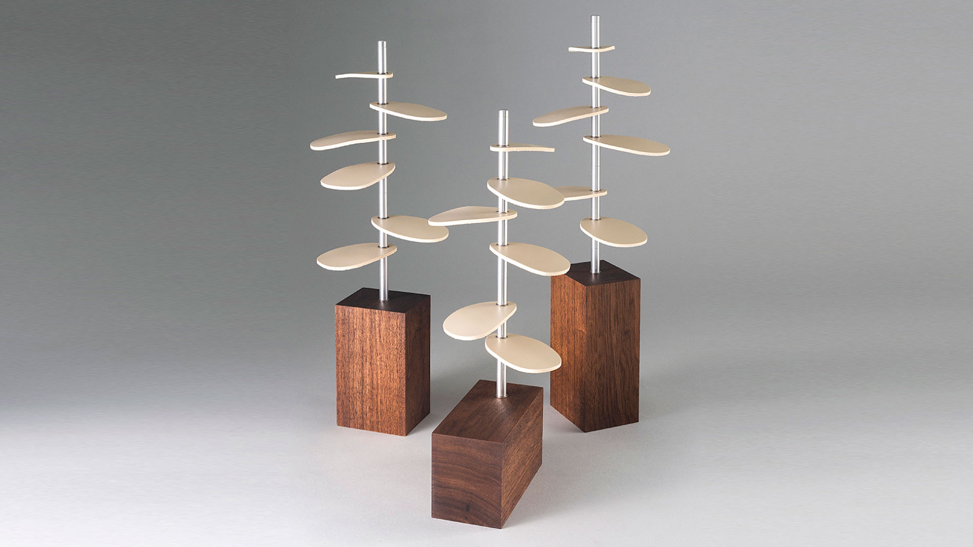 trio of tree-shaped design pieces with wood bases, metal stems, and white leather leaves.
