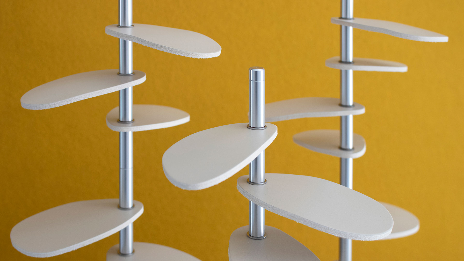 Closeup of trio of tree-shaped design pieces with wood bases, metal stems, and white leather leaves against a yellow background