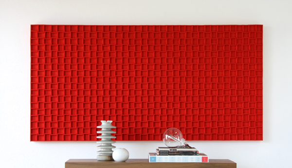 Large rectangular red felt panel with grid pattern hanging behind a table with knick knacks