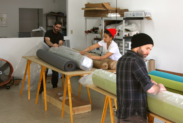 Three people removing the plastic wrapping on bolts of felt