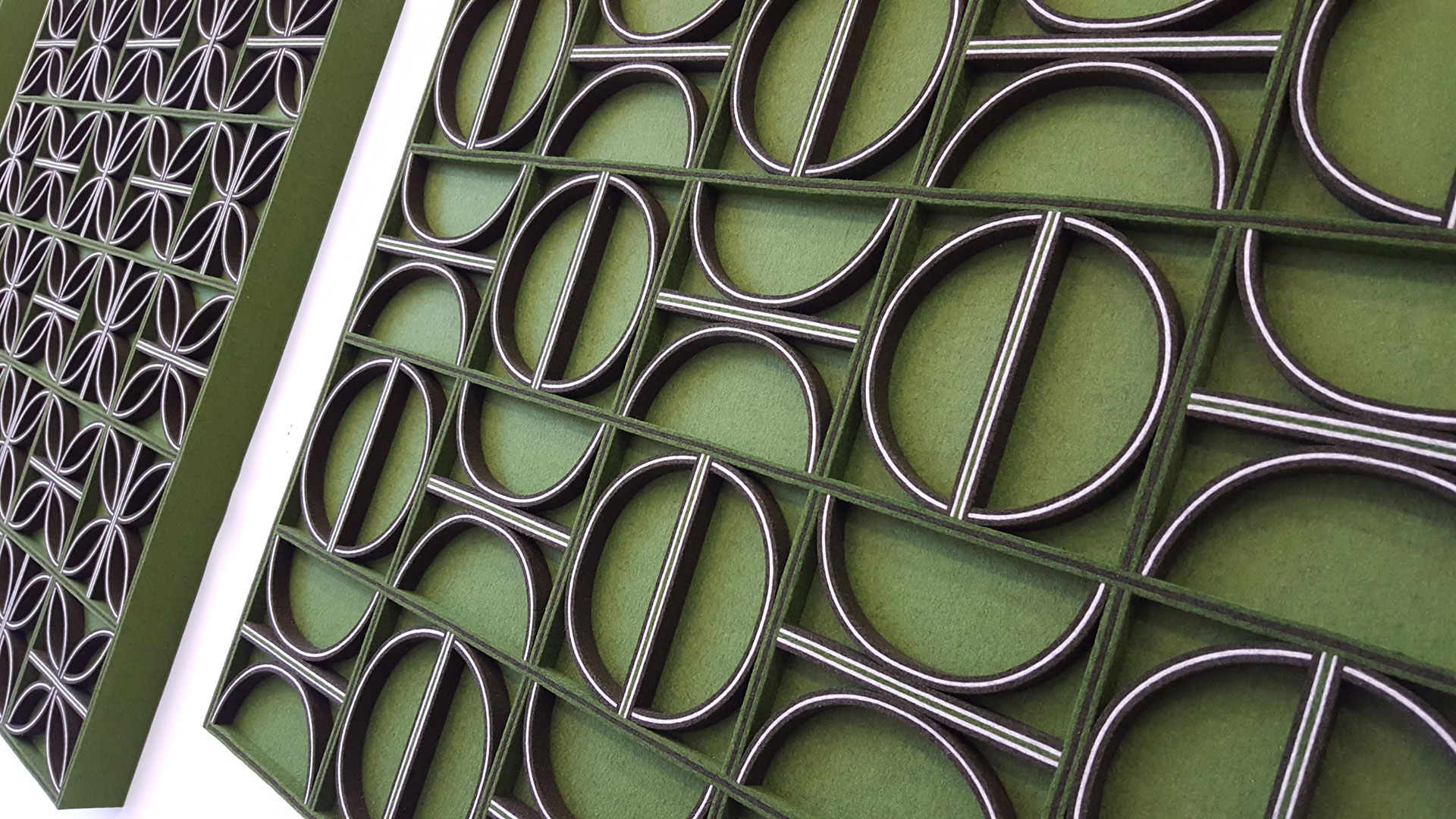 Closeup of a green felt wall panel with circle, half circle and straight lines creating a modern pattern with brown and white accents