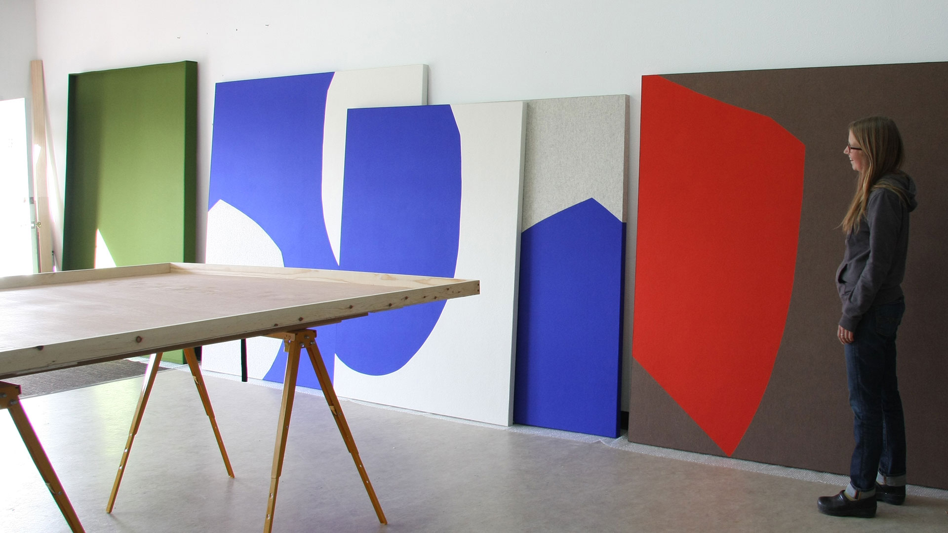 A woman with long hair looks at a grouping of large felt canvas with organic shapes in blue, red and green