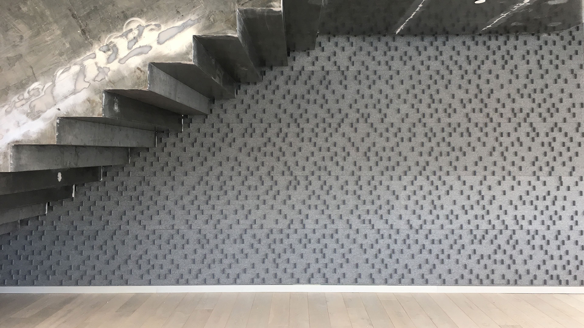 A gray felt wall with short vertical felt tabs seen under a staircase