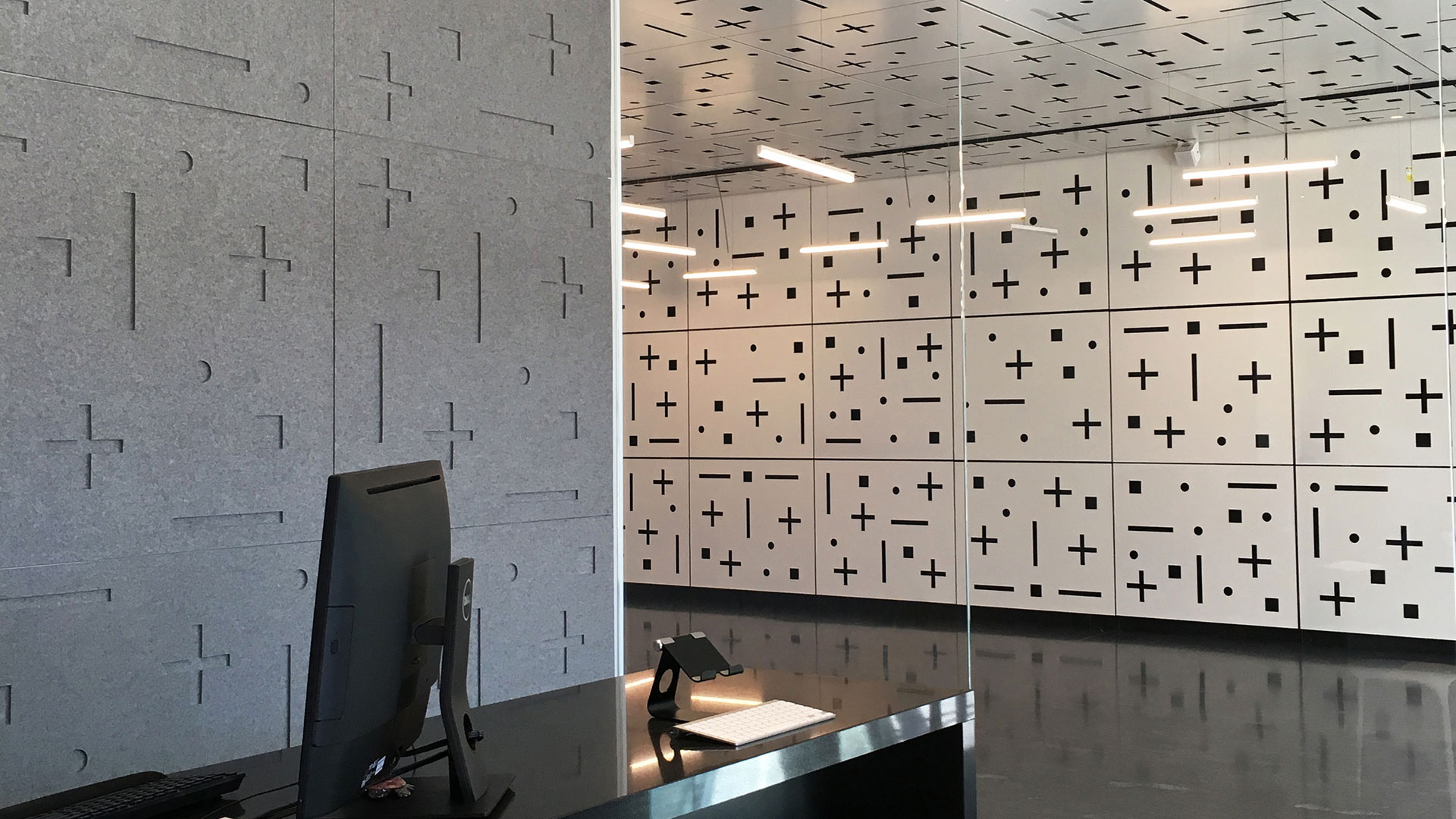 Gray wall covering at left with plus and minus pattern. The lobby to the right has a wall with a similar pattern in black and white