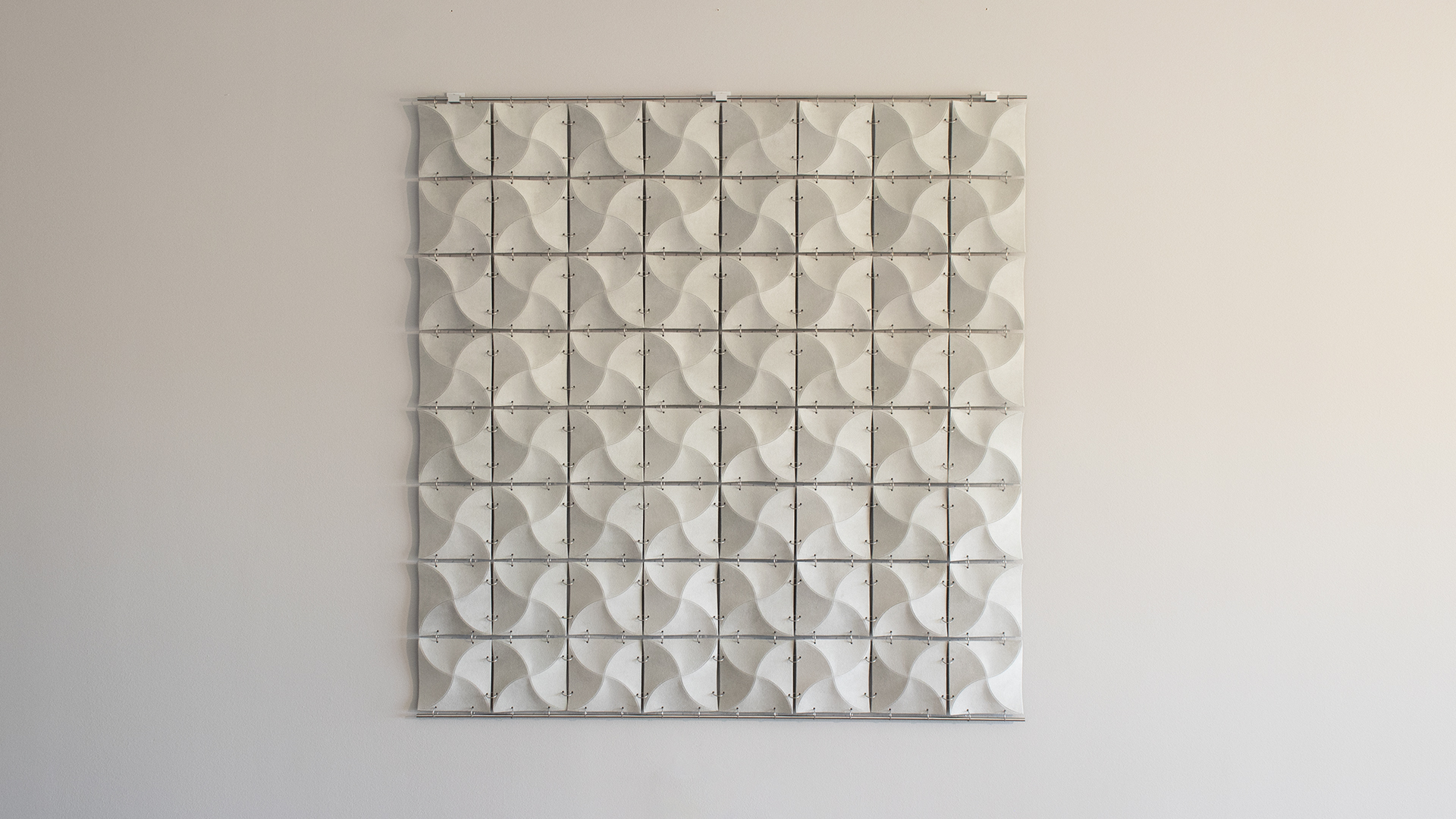 Gray suede square wall hanging constructed of many smaller wavy squares connected with metal rings