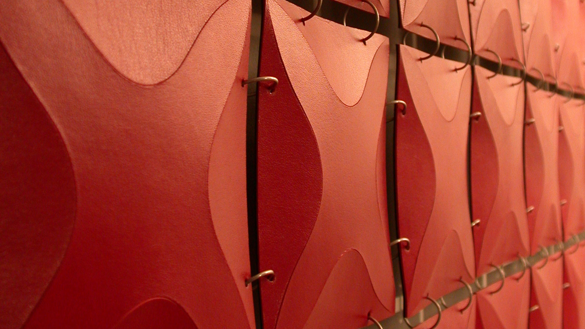 Closeup of red leather wall hanging constructed of many smaller 3 dimensional x-pattern squares connected with metal rings