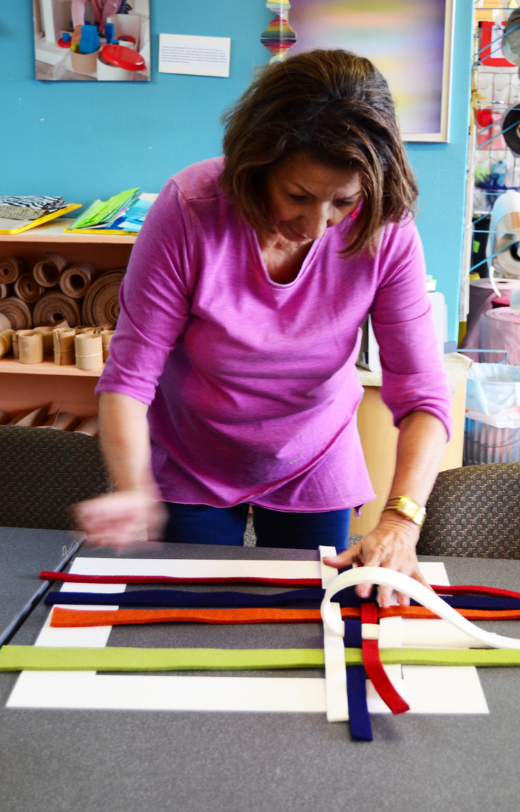 A woman with dark hair and a pink shirt working with color strips of wool felt