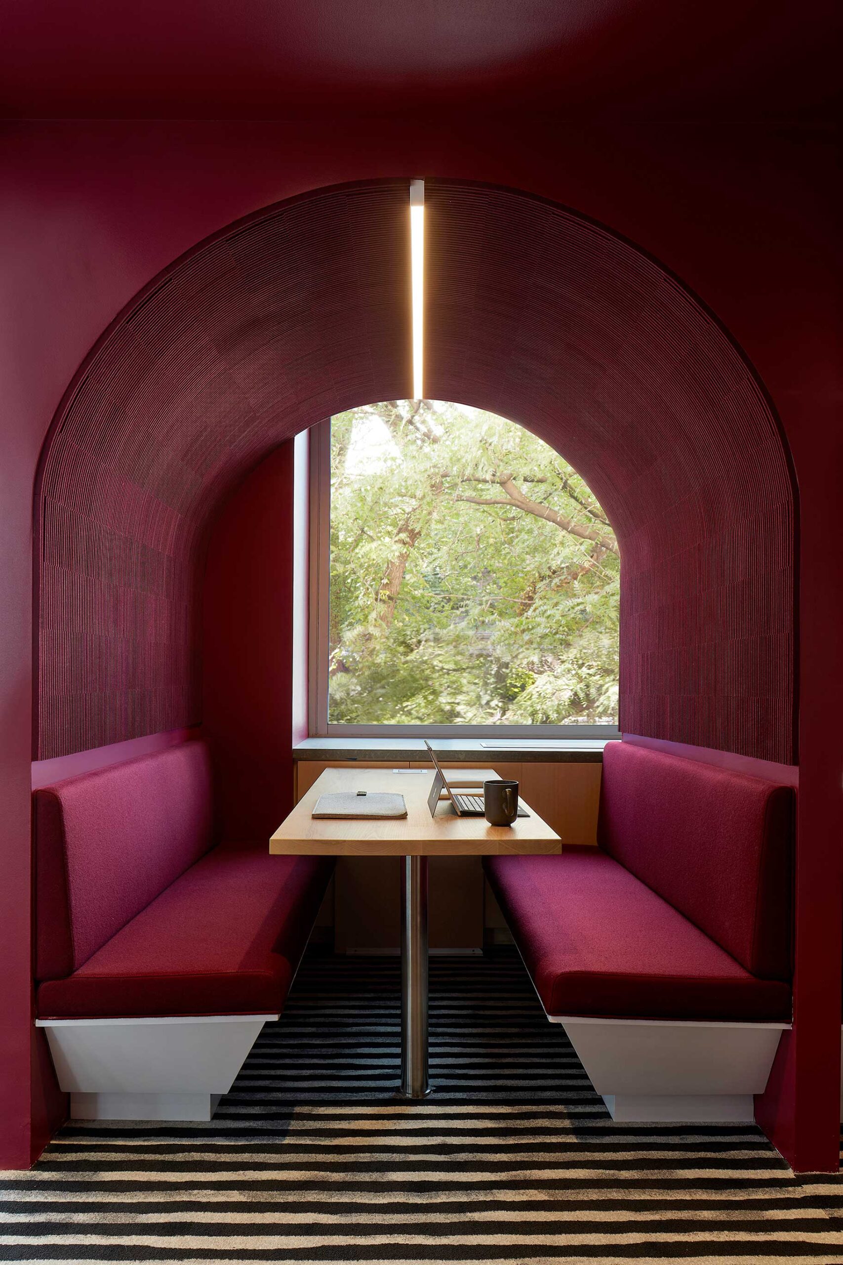 fuschia booth set into an arched curvalinear enclosure with filzfelt submaterial ribsy wallcovering in a deep wine color lining the arch for sound dampening