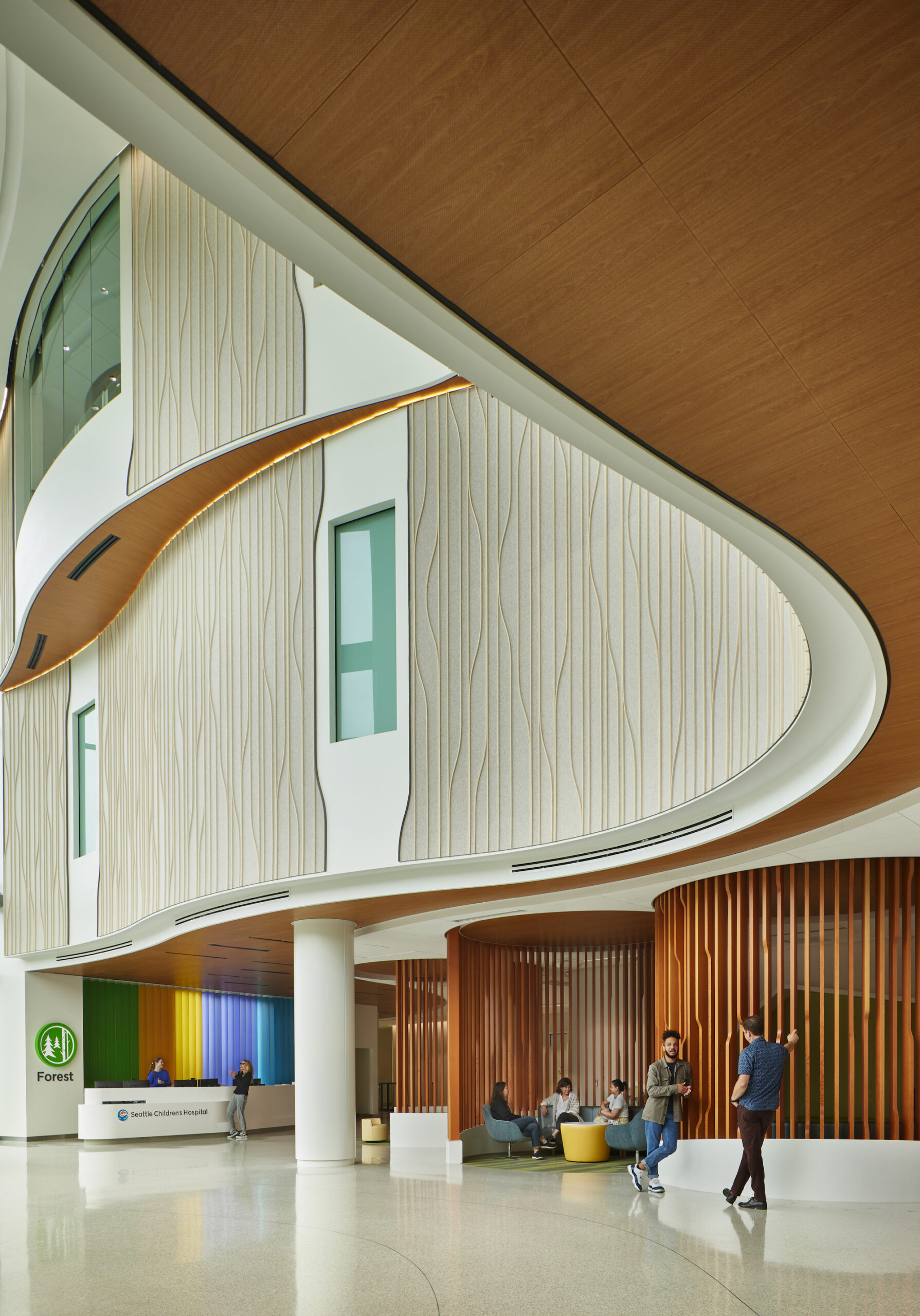 The tall lobby of a hospital. The second and third stories have curved walls covered in a white tan detailed felt wall covering