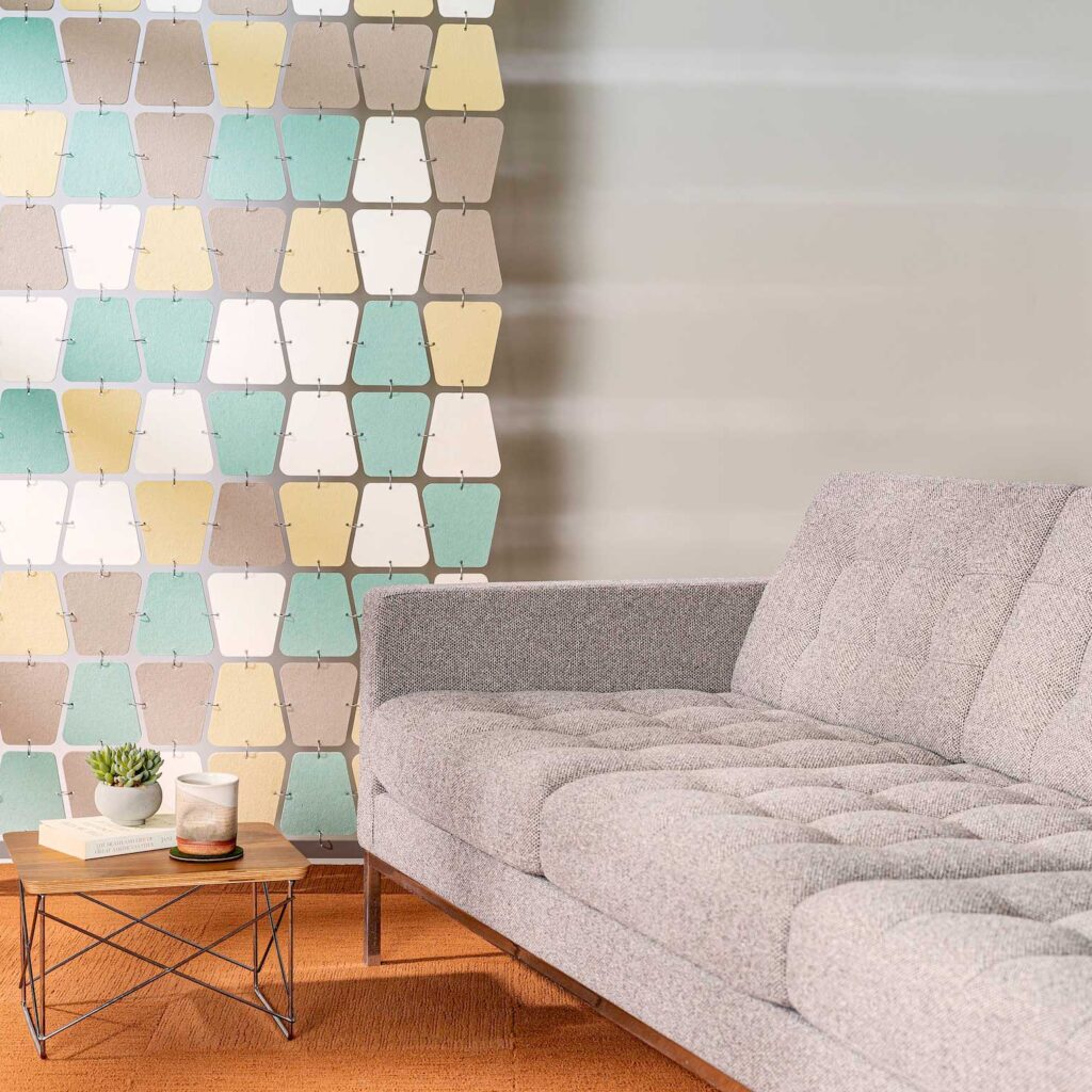 multicolor felt room divider in teal, white, yellow and brown hangs next to a couch modern couch