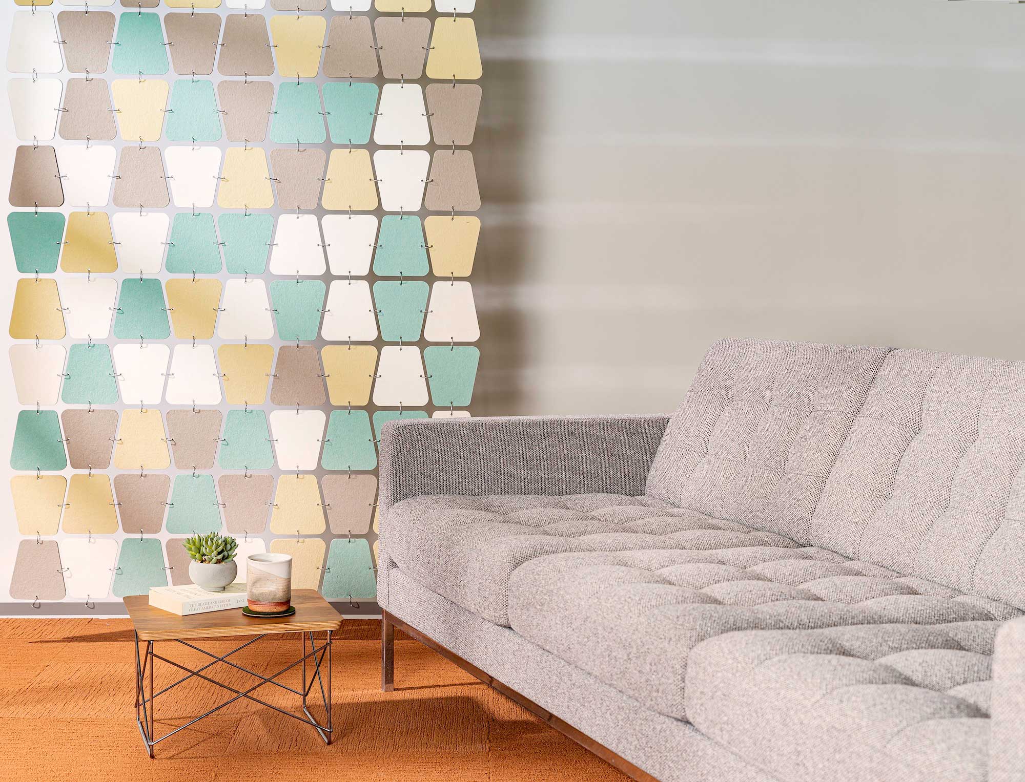 multicolor felt room divider in teal, white, yellow and brown hangs next to a couch modern couch