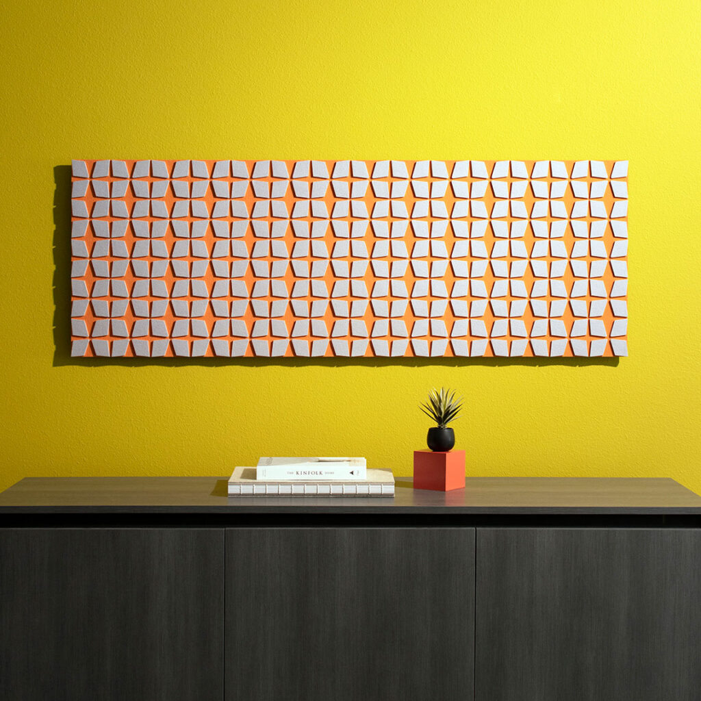 A long rectangular wall art piece hangs on a chartreuse wall. The piece has repeating diamond shapes in gray and the background felt is a bight orange.