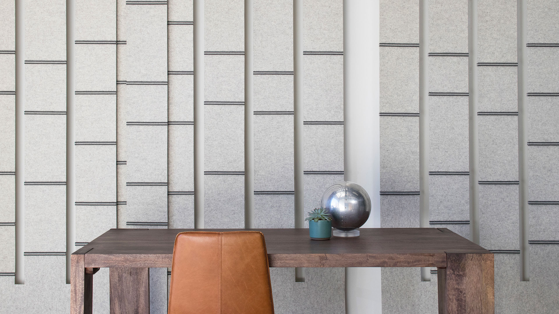 Light gray felt screens in stripes with occasional dark horizontal stripes hang behind a wood desk