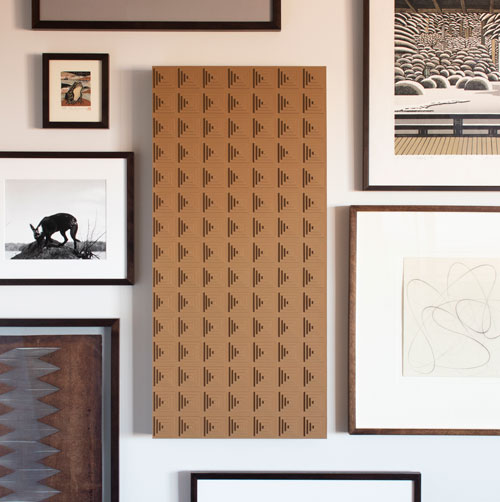 A tan leather rectangle with built up small squares hung vertically on a wall with other art works.