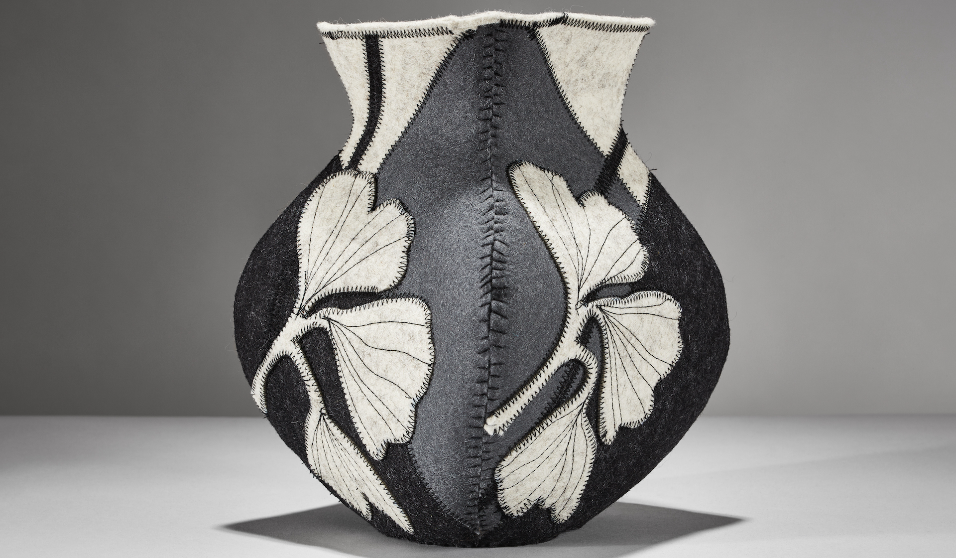 gray neutral vessel made from wool felt with a ginkgo leaf emblem