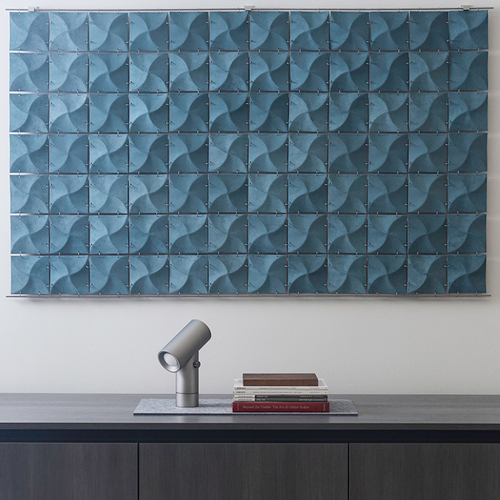 A wall hanging made from squares of blue ultrasuede bent to create dimensionality and shadow hangs behind a credenza and a table lamp