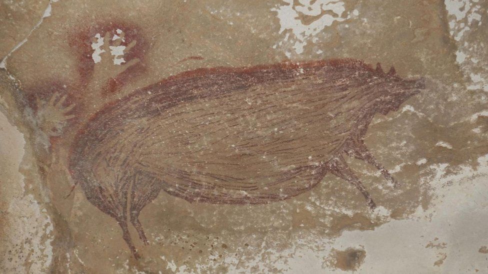 cave painting of a boar with red outlined handprints