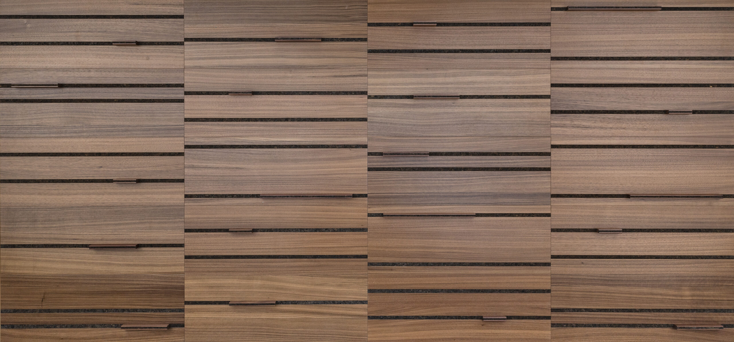 A closeup of a walnut wood wall covering with horizontal lines inlaid with a dark cork. Horizontal bars of various lengths are inset in the cork lines.