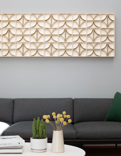 felt wall art with a white background and brown curbed and straight lines hangs over a gray couch with a coffee table in front