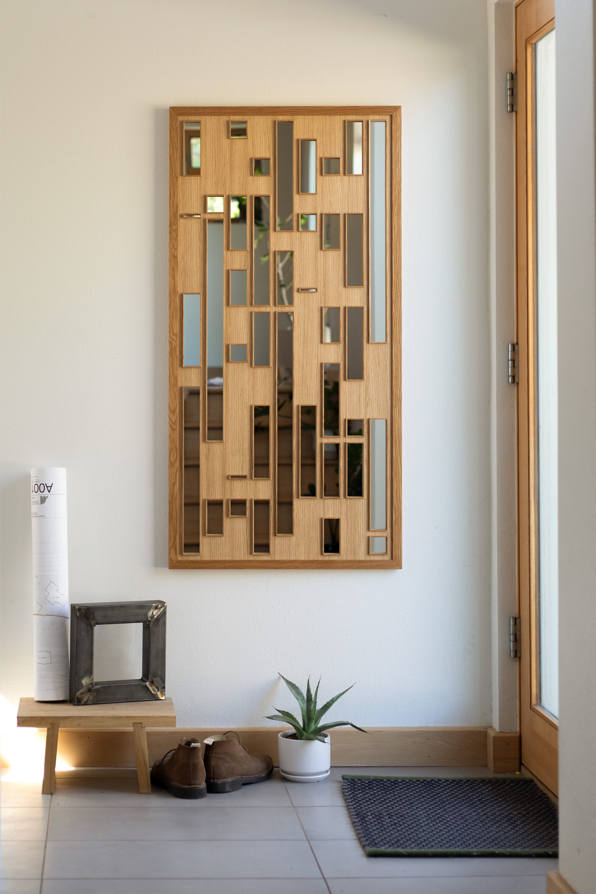 an entryway to a house. next to the door is a tall mirror with a wooden framing and various lengths of rectangular cutouts that show mirror through the framing.