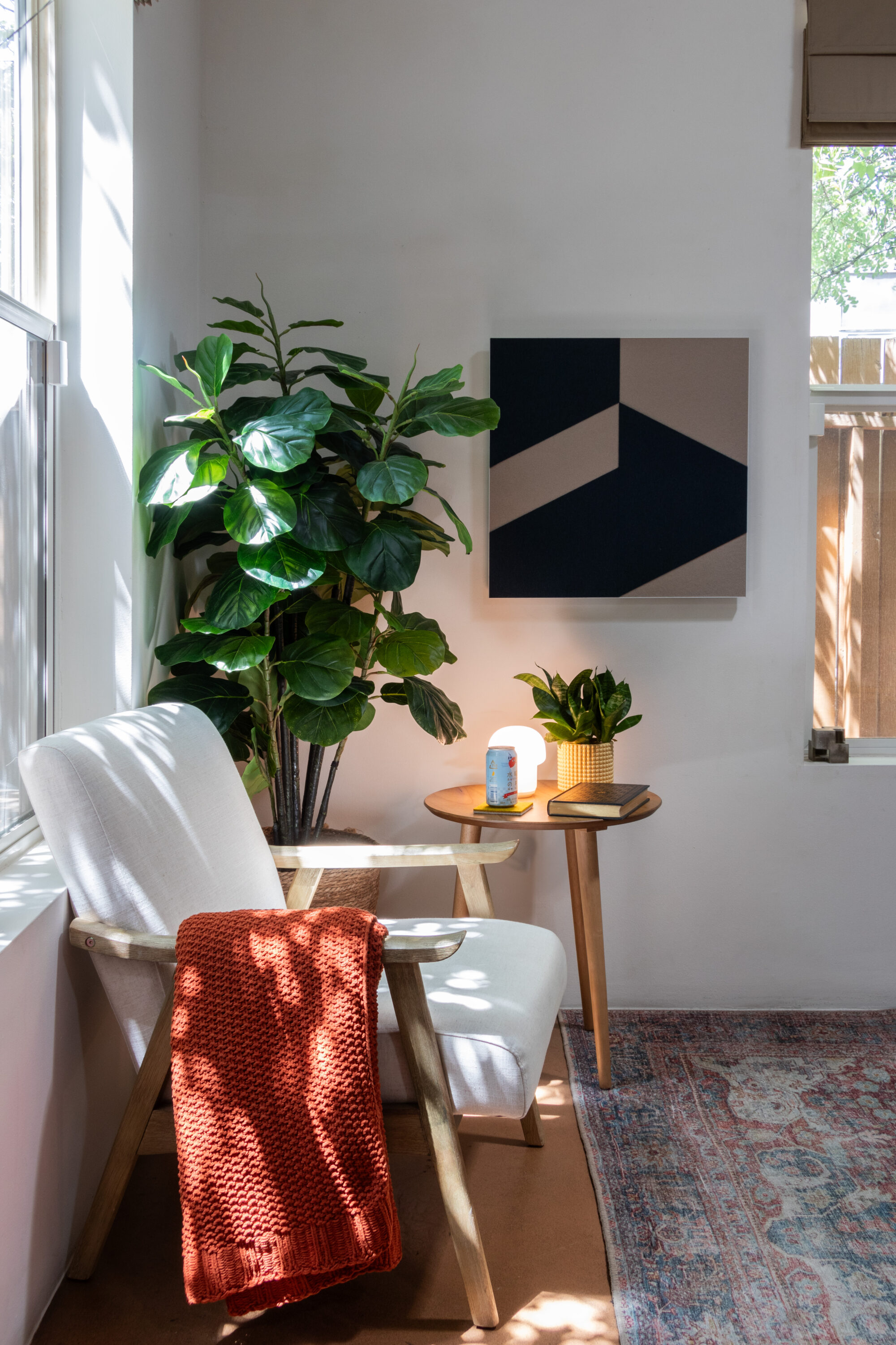 A square wool felt wall art panel with gradient strips from dark to light and narrow to wide from left to right on the panel. It is hung on a chartreuse wall with a cabinet with a basket and books on it.